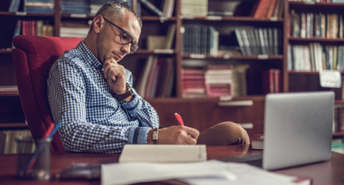 Male lecturer taking notes in home office.