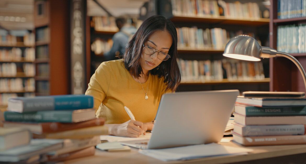 Young lady sitting in the library using a laptop to do copywriting.