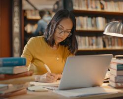 Young lady sitting in the library using a laptop to do copywriting.