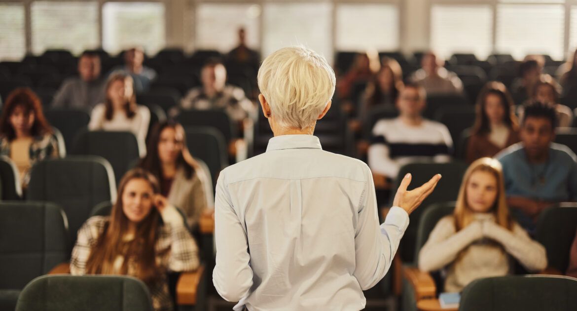 Back view of a female professor teaching her students at lecture hall.