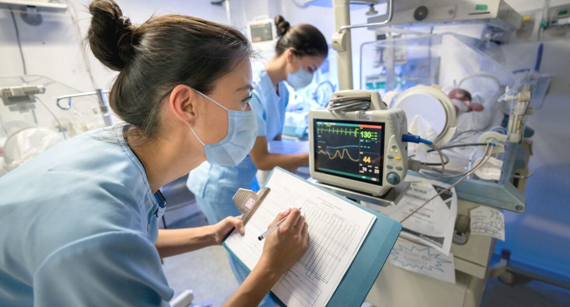 Nurse monitoring a premature newborn in an incubator while wearing a facemask